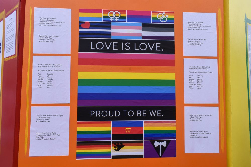 A display with various LGBTQ pride flags alongside the words "Love is love. Proud to be we."